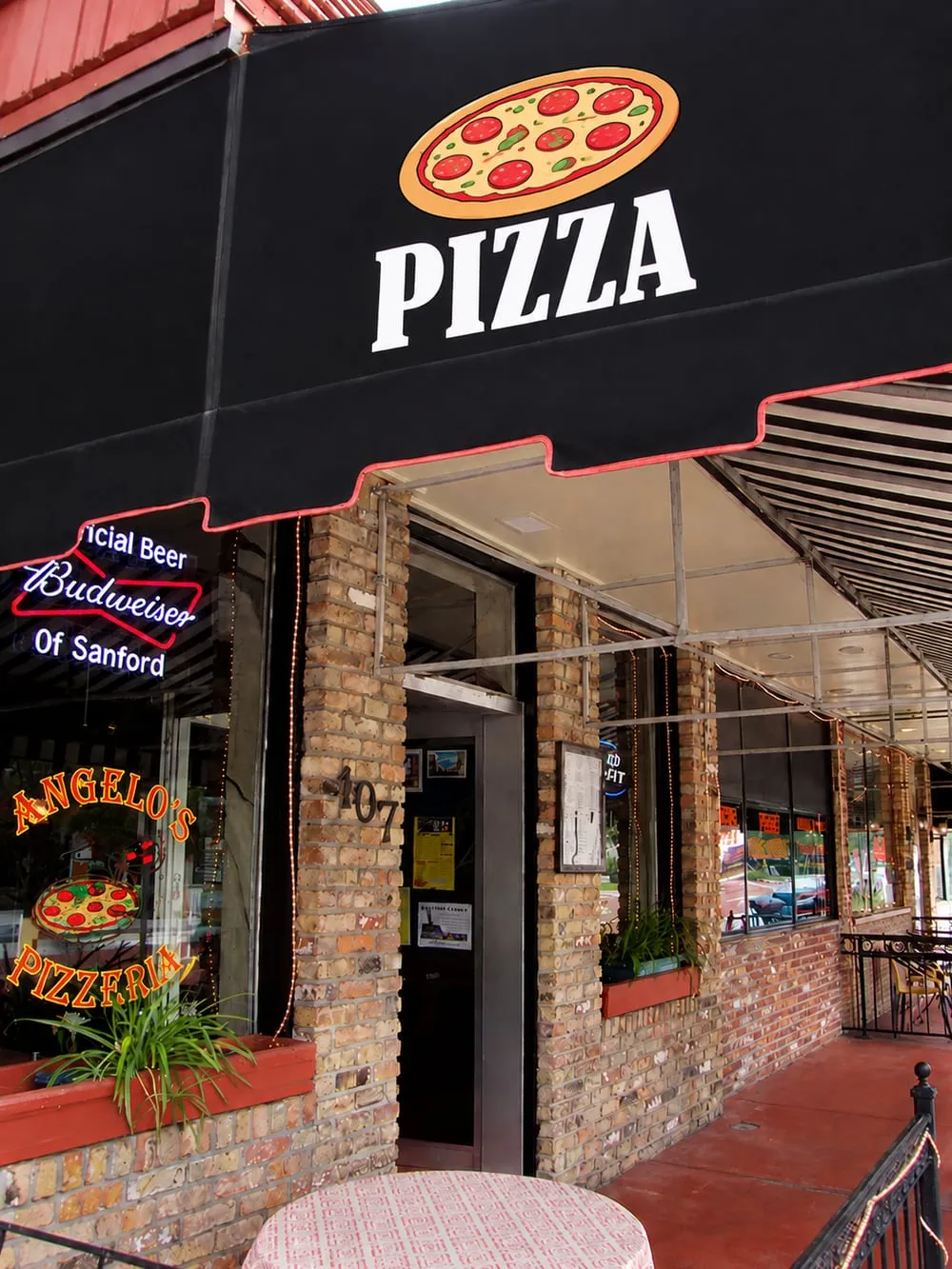 Angelo's Pizzeria at 107 West First Street in Sanford, a black pizza awning over the brick storefront and a Budweiser neon in the window